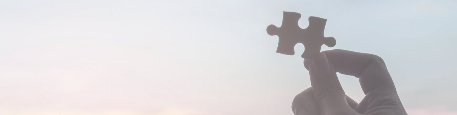 Hand hält ein Puzzleteil gegen den Himmel